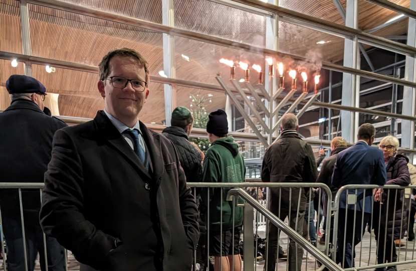 Joel standing outside the Senedd with the Menorah lit in the background