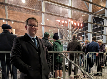 Joel standing outside the Senedd with the Menorah lit in the background